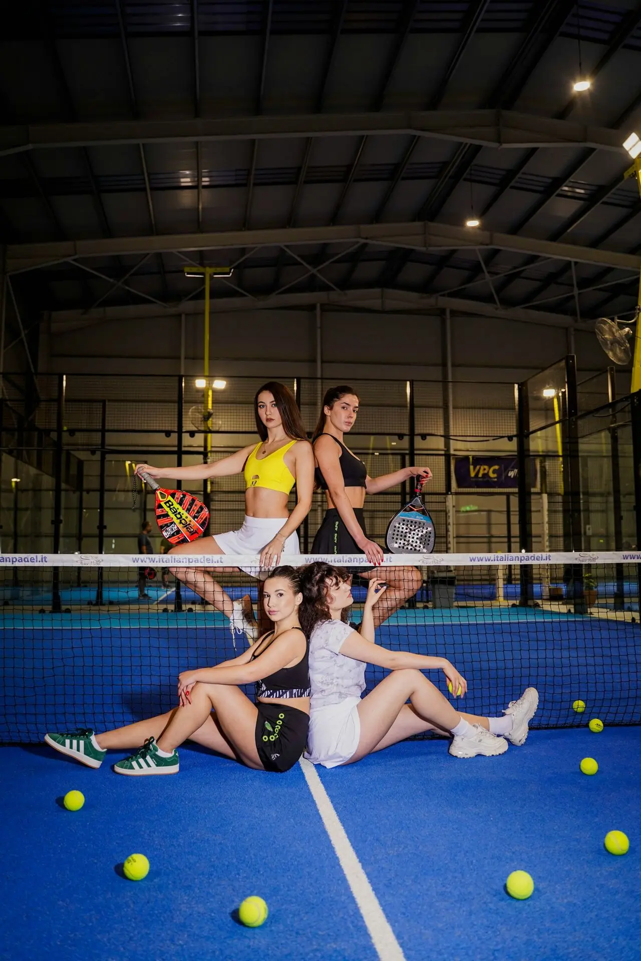 Four women posing on a blue padel court with racquets.